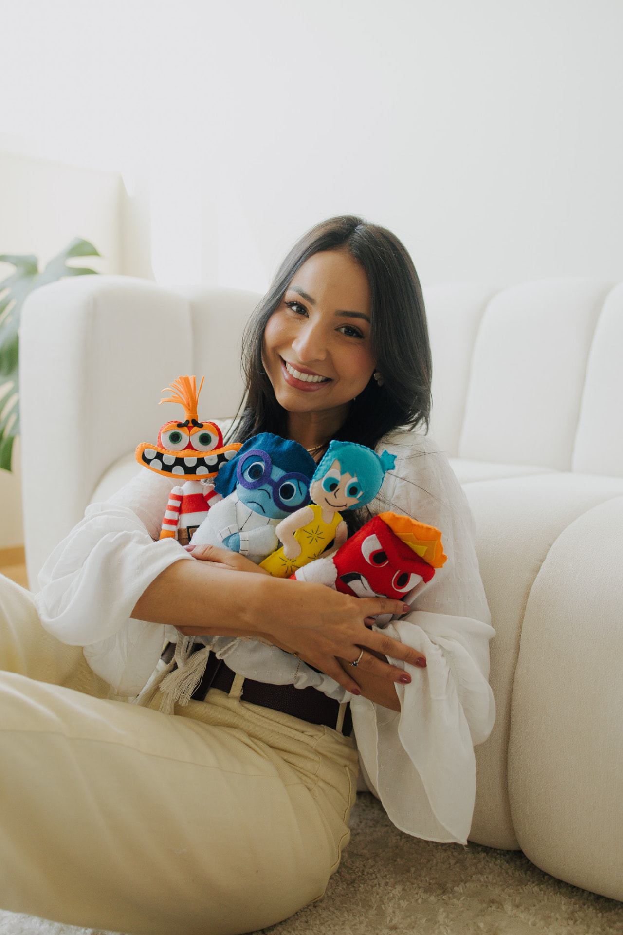 Jarliny Souza sorrindo, sentada em um sofá com bonecos que representam as emoções